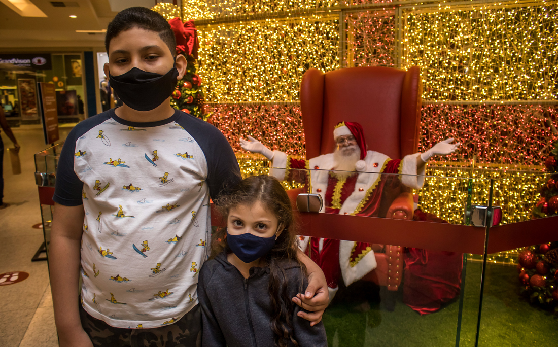 Papai Noel deu um jeitinho de aparecer durante a pandemia. O bom velhinho fica protegido atrás de um muro de vidro.